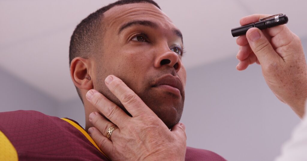 Doctor using pen light to check eyes of football player