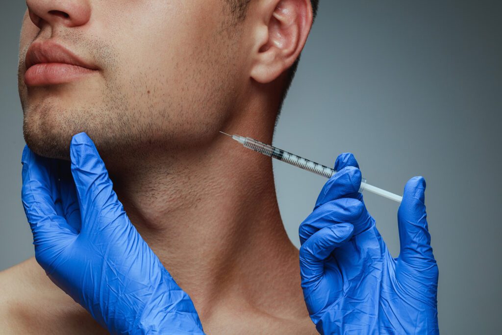 Close-up portrait of young man isolated on grey studio background. Filling botox surgery procedure. Concept of men's health and beauty, cosmetology, self-care, body and skin care. Anti-aging.